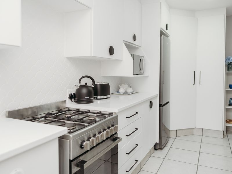 A modern, well-maintained kitchen featuring white cabinetry, stone countertops, a gas stove with oven, and a stylish scalloped tile backsplash.