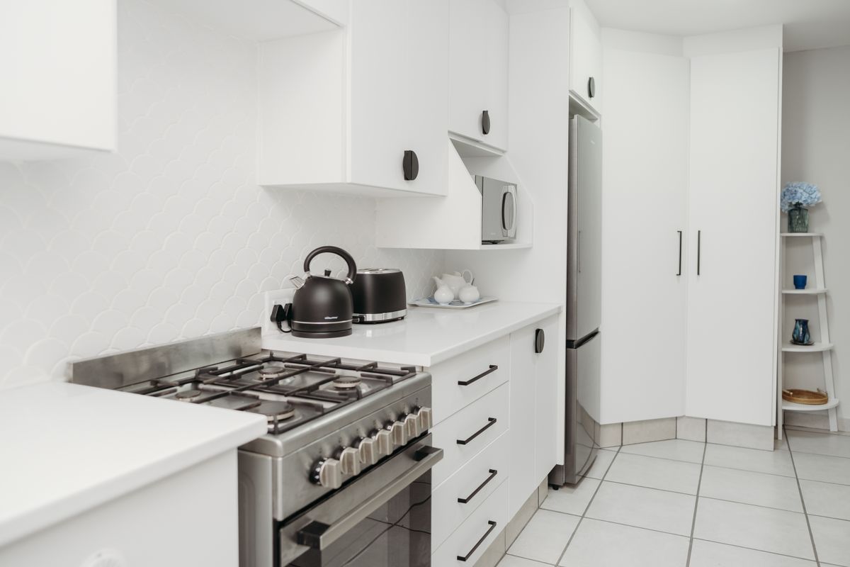 A modern, well-maintained kitchen featuring white cabinetry, stone countertops, a gas stove with oven, and a stylish scalloped tile backsplash.