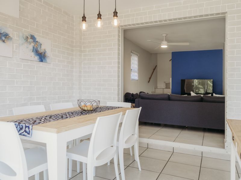 Open plan dining area featuring exposed brick walls and tiled flooring, flowing into a connected living space with a ceiling fan.