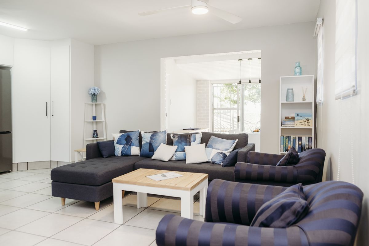 A bright and well-maintained living room featuring neutral tiled flooring, a ceiling fan, and integrated storage cabinetry, offering a comfortable and functional living space.
