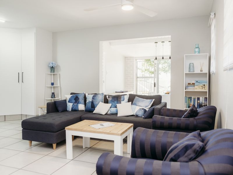 A bright and well-maintained living room featuring neutral tiled flooring, a ceiling fan, and integrated storage cabinetry, offering a comfortable and functional living space.