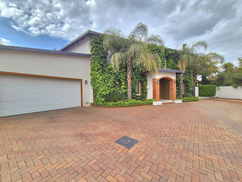 Front elevation of a house featuring a brick paved driveway, double garage, and an arched entrance with climbing ivy facade.