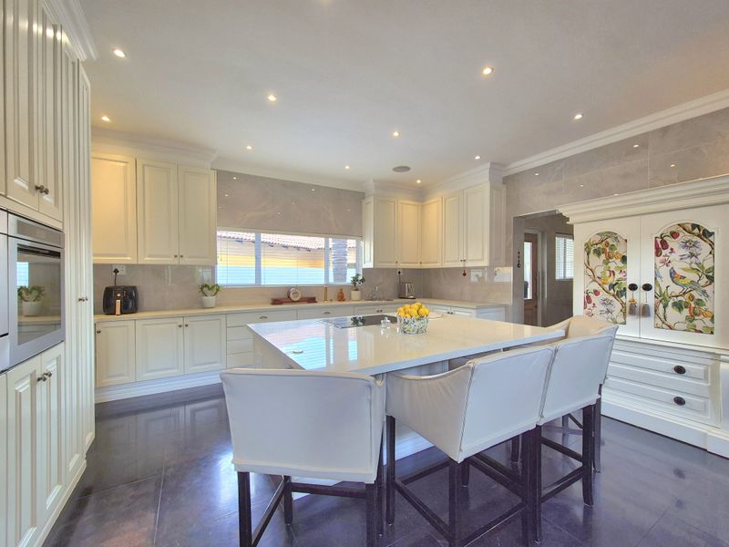 A modern, well-appointed kitchen featuring white cabinetry, stone countertops, a central island with seating, and high-quality finishes throughout.