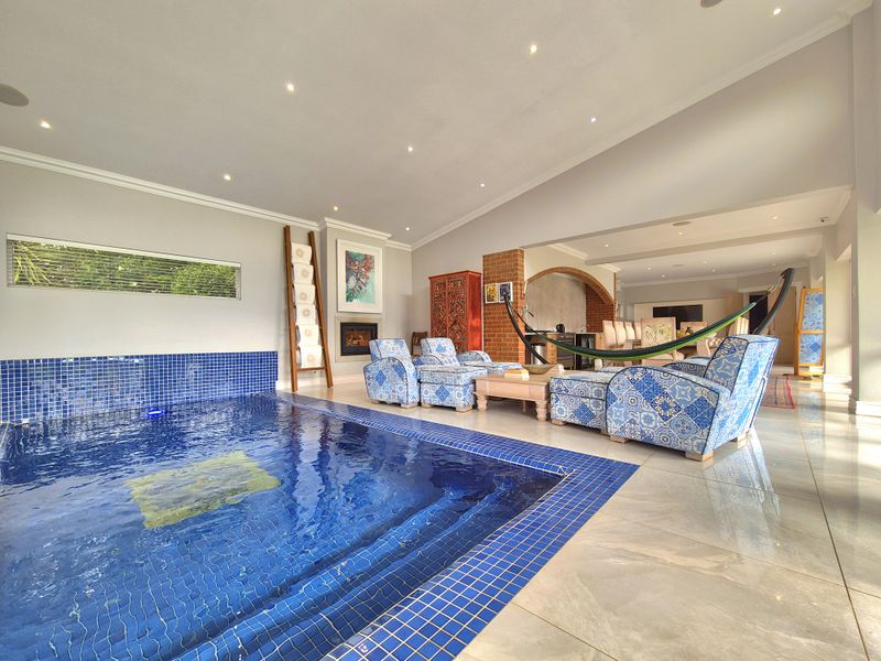 A unique indoor pool area featuring a tiled swimming pool, recessed lighting, and a brick fireplace, seamlessly connected to the adjacent living space.