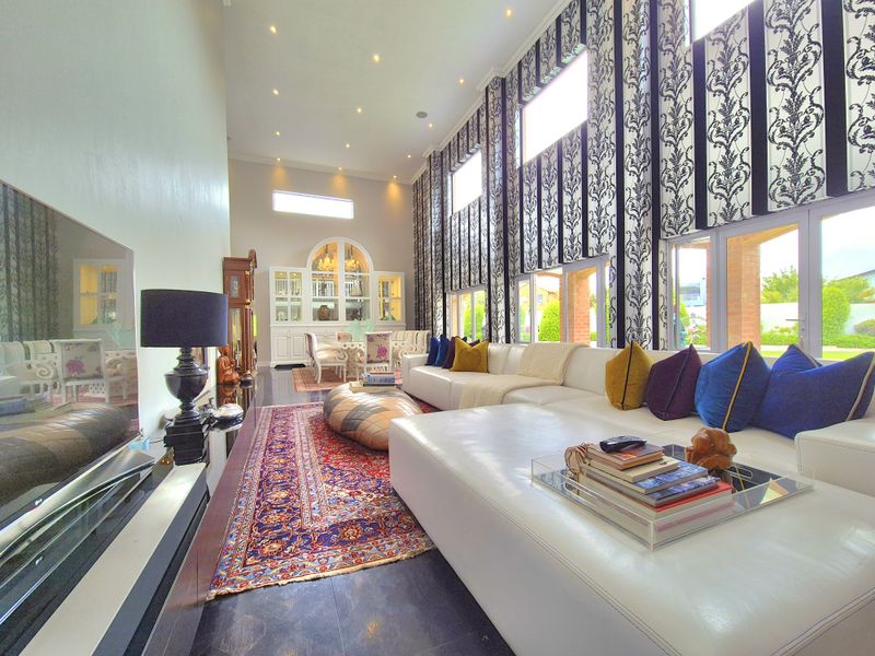 Spacious living room featuring high ceilings, large windows with decorative curtains, built-in display cabinetry, and polished tiled flooring.