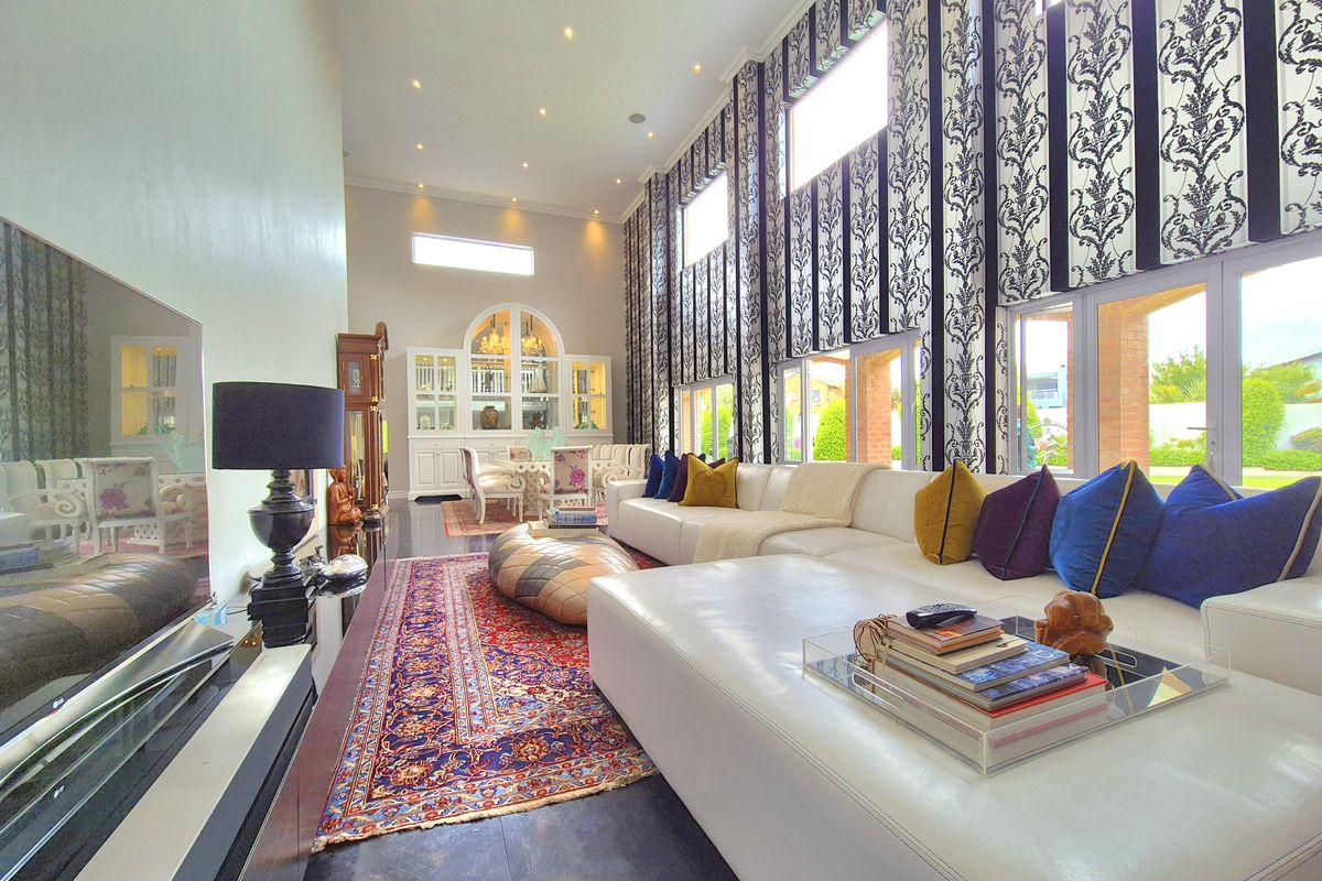 Spacious living room featuring high ceilings, large windows with decorative curtains, built-in display cabinetry, and polished tiled flooring.