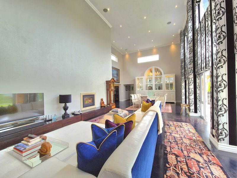 Spacious open-plan living and dining area featuring double-height ceilings, large windows, built-in fireplace, and elegant custom display cabinetry.