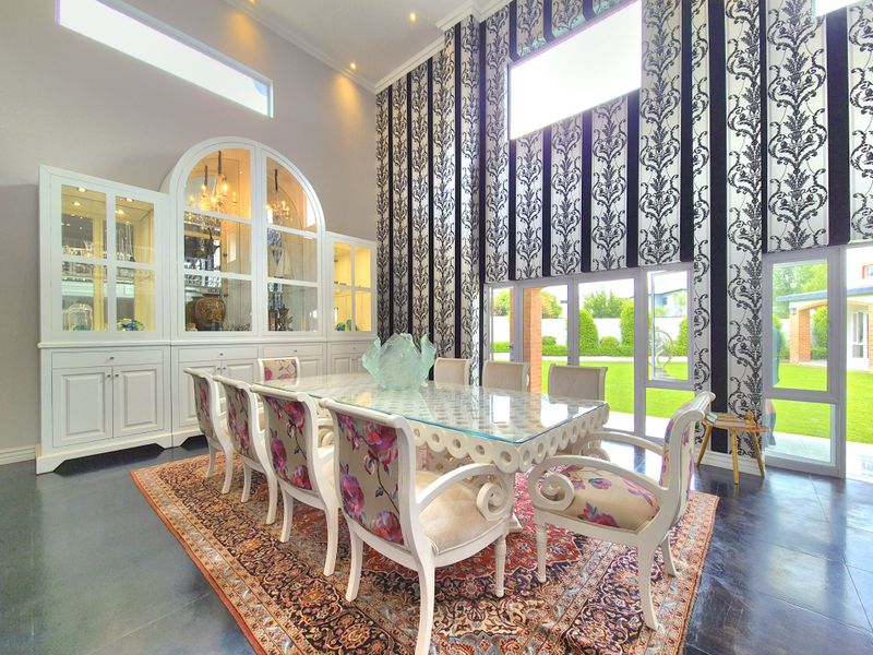 Elegant dining room featuring double-height ceilings, clerestory windows, built-in display cabinetry, and polished concrete floors with direct access to the garden.