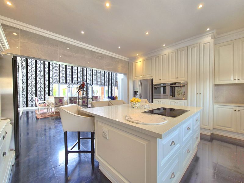Modern kitchen featuring a large central island with stone countertops, integrated appliances, and ample cabinetry, seamlessly flowing into an adjacent living area.