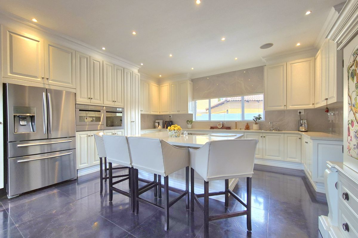 A modern, well-appointed kitchen featuring white cabinetry, a central island with stone countertops, integrated appliances, and recessed lighting throughout.