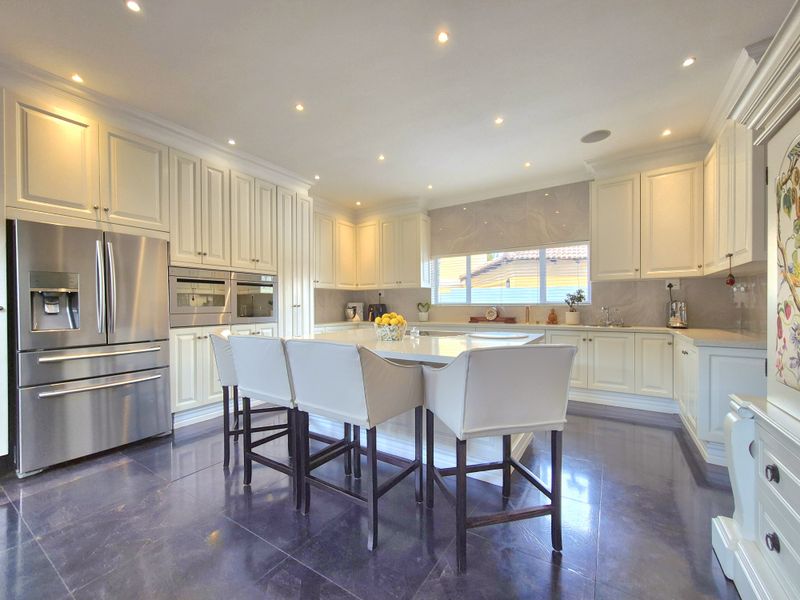 A modern, well-appointed kitchen featuring white cabinetry, a central island with stone countertops, integrated appliances, and recessed lighting throughout.