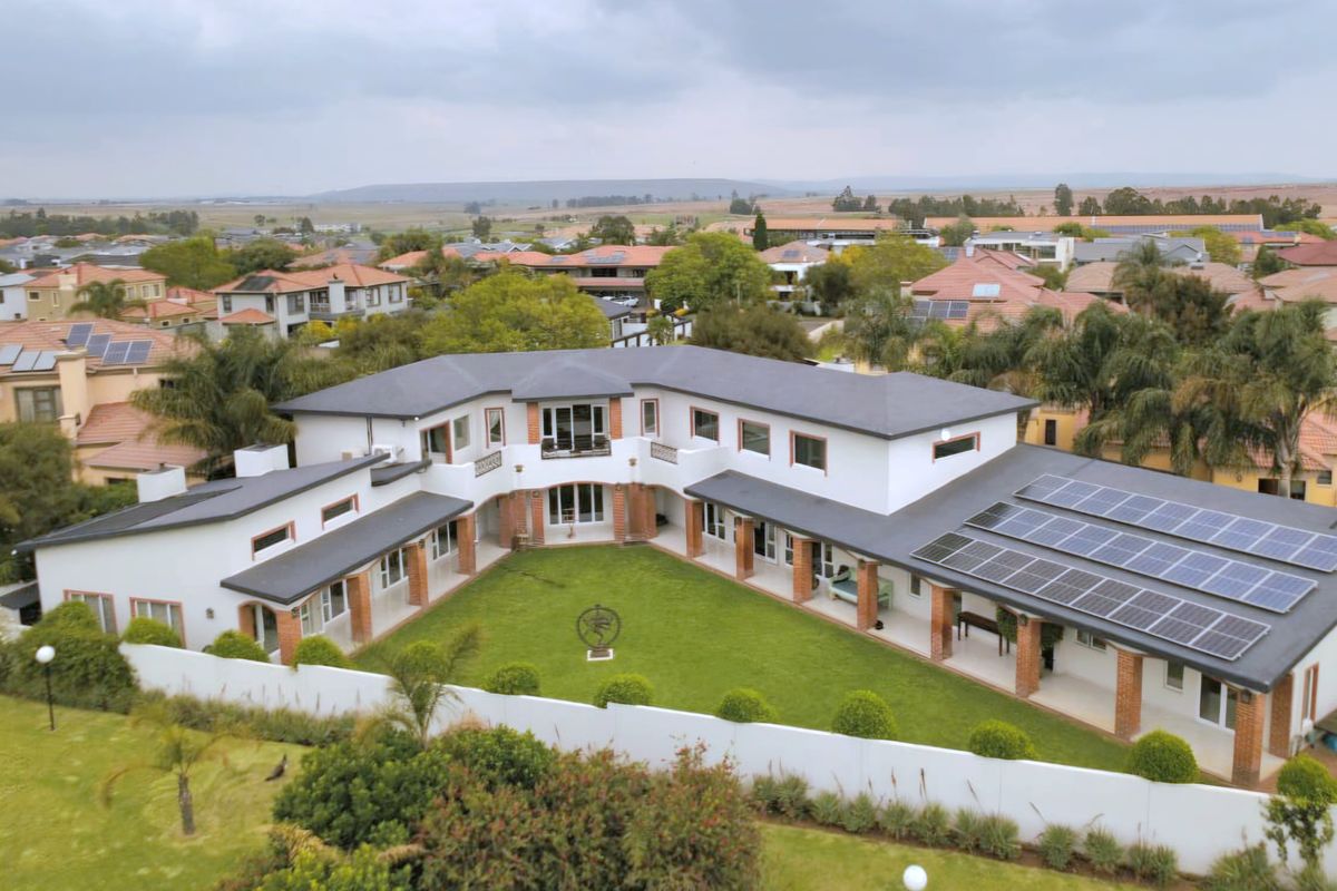 Aerial view of a large U-shaped residential property featuring a central lawn, covered patio areas, and extensive roof-mounted solar panel arrays.