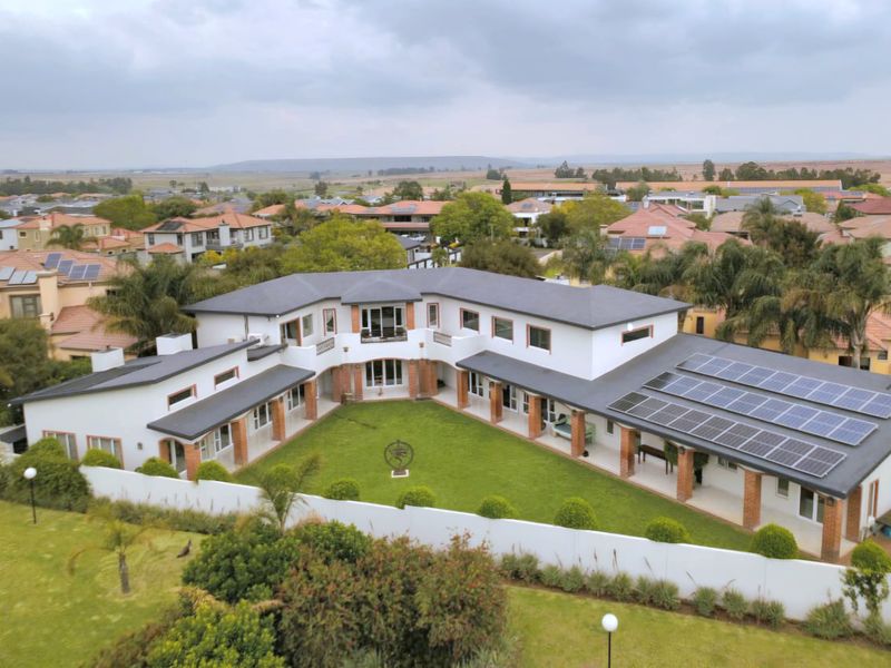 Aerial view of a large U-shaped residential property featuring a central lawn, covered patio areas, and extensive roof-mounted solar panel arrays.