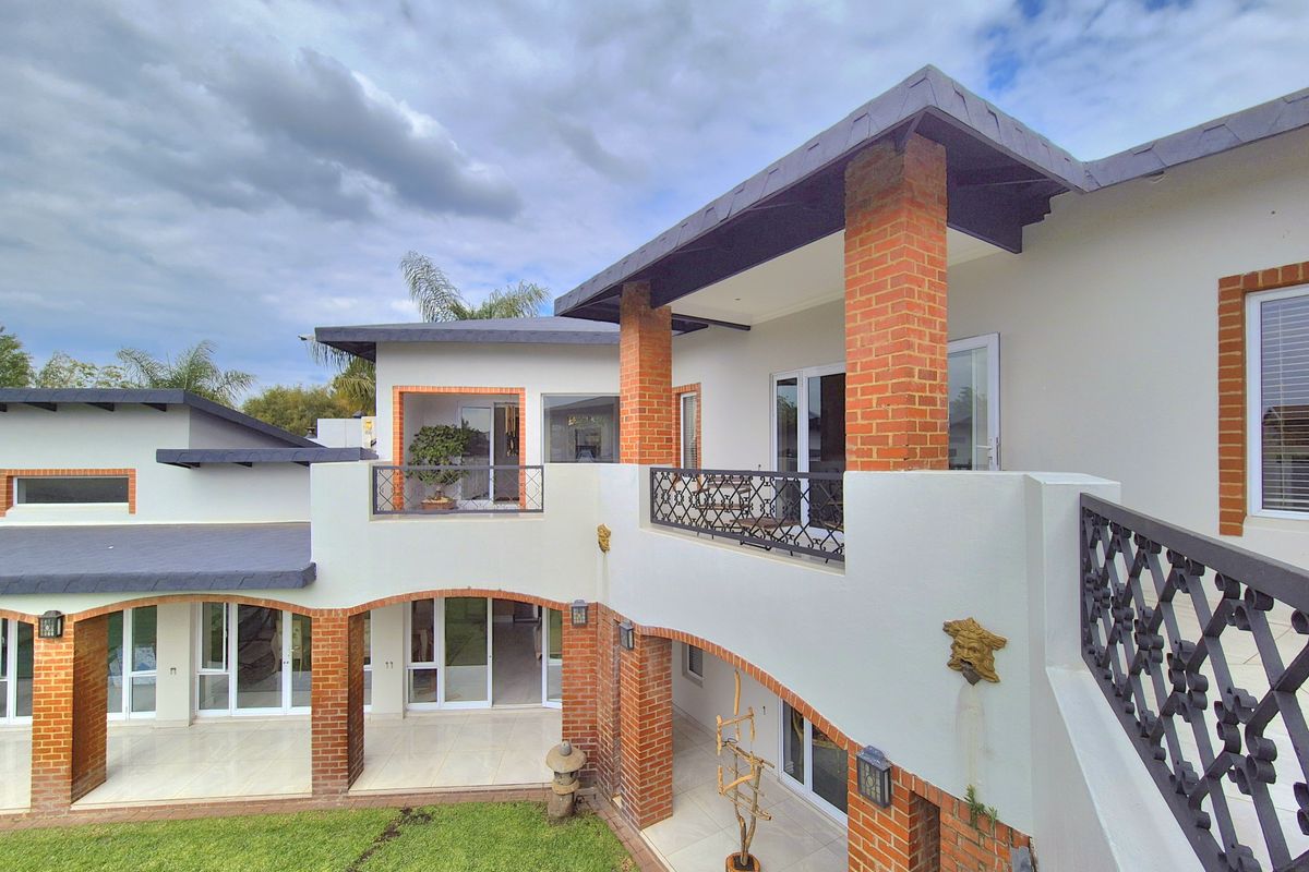 Rear view of a multi-level home featuring brick pillars, wrought iron railings, and spacious tiled patios overlooking a well-maintained garden.