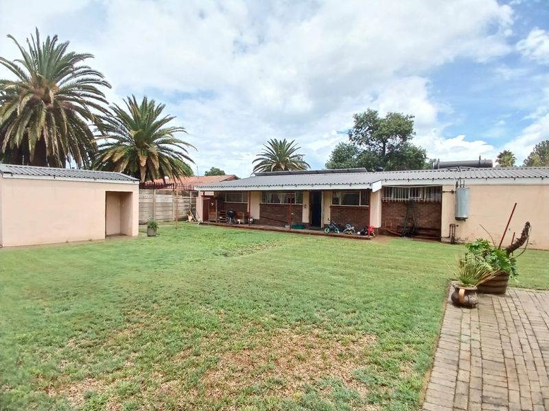 Rear view of the property featuring a spacious lawn, paved walkway, detached outbuilding, and brick facade with a metal roof.
