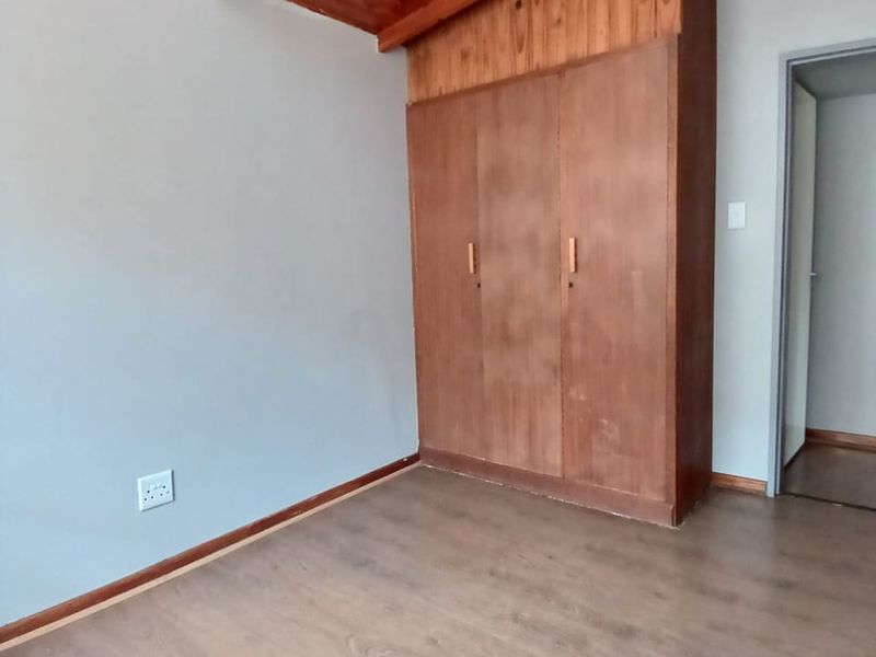 A vacant bedroom featuring laminate flooring, a built-in wooden wardrobe, and an exposed timber rafter ceiling.