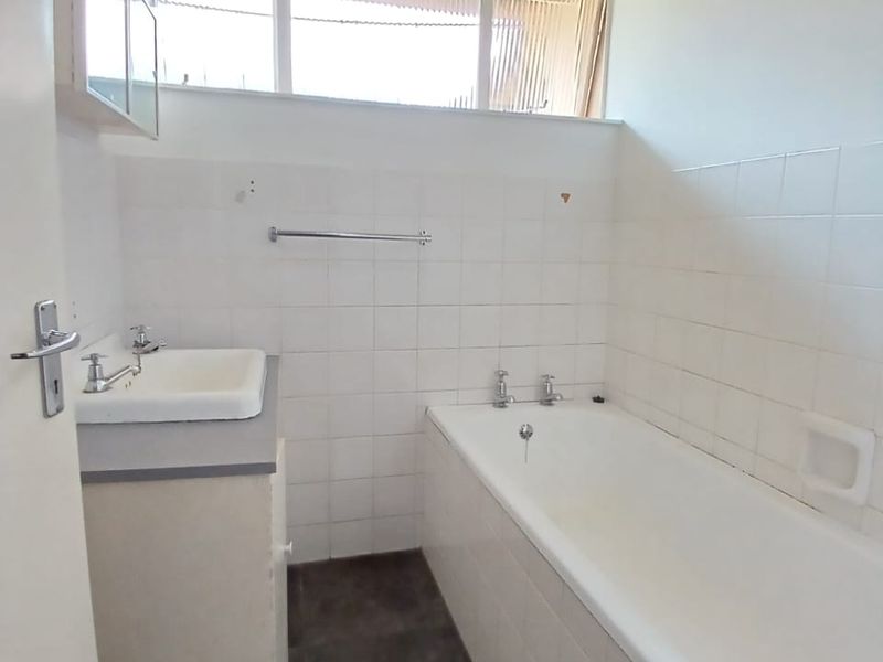 A functional bathroom featuring a built-in vanity, bathtub, and tiled walls under a timber ceiling, offering potential for modern renovation.