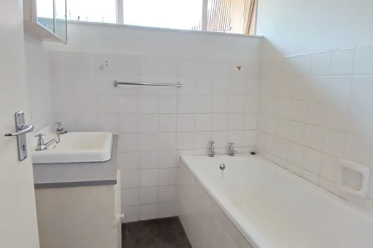 A functional bathroom featuring a built-in vanity, bathtub, and tiled walls under a timber ceiling, offering potential for modern renovation.