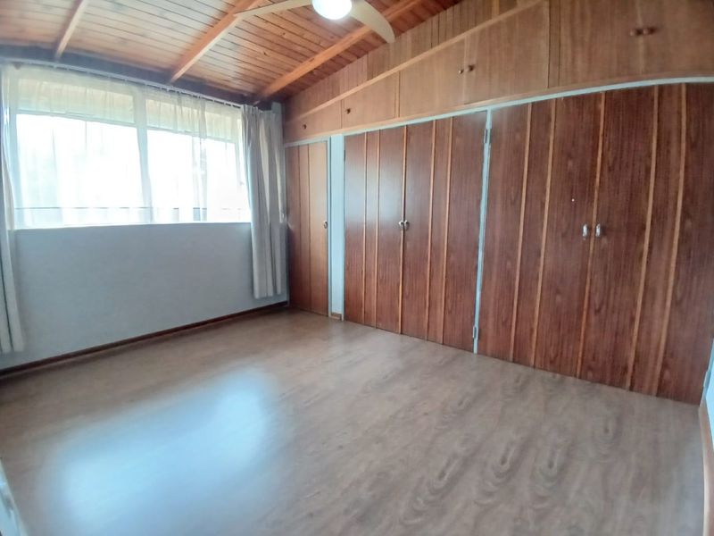 A spacious bedroom featuring warm timber ceilings, laminate flooring, and extensive built-in cupboard storage, offering a clean and functional living space.
