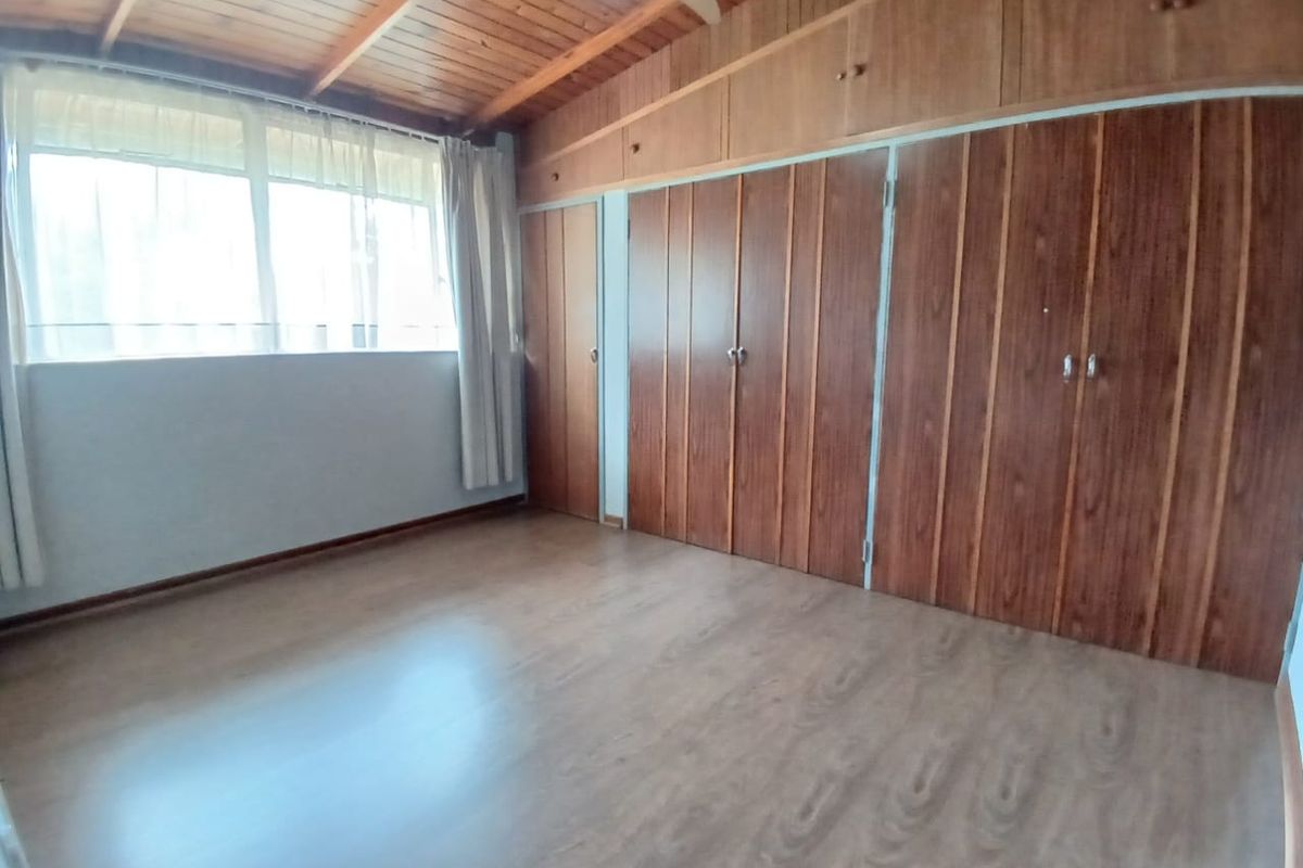A spacious bedroom featuring warm timber ceilings, laminate flooring, and extensive built-in cupboard storage, offering a clean and functional living space.