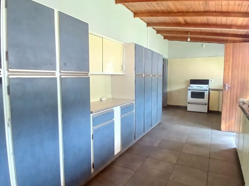 Spacious kitchen featuring extensive built-in cabinetry, tiled flooring, and a rustic exposed timber beam ceiling, offering a functional layout with a freestanding stove.