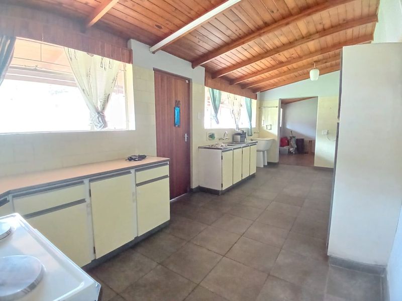 A functional kitchen featuring exposed timber ceilings, tiled flooring, and ample built-in cabinetry with a double sink, offering potential for modern renovation.
