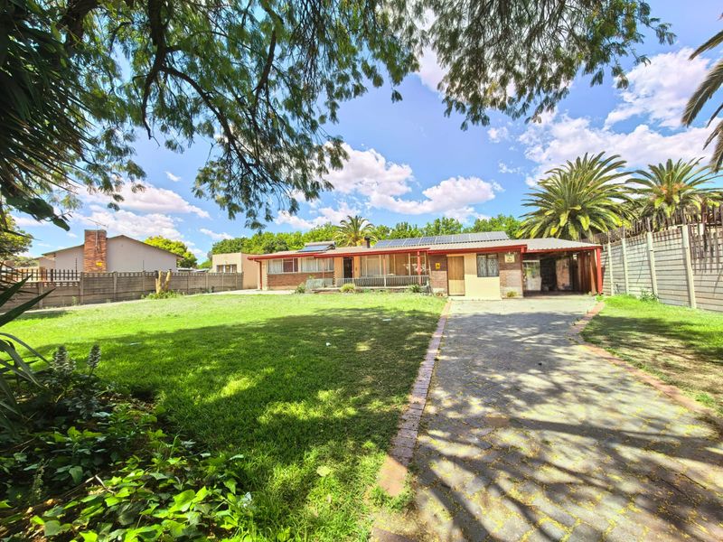 Front view of the property featuring a spacious lawn, paved driveway, carport, and solar panels installed on the roof.