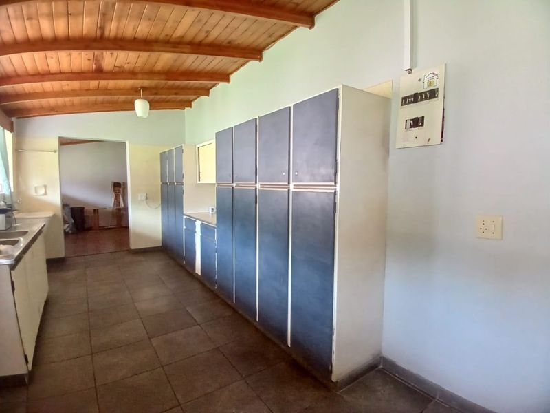 A spacious kitchen featuring extensive built-in cabinetry, tiled flooring, and a distinctive exposed timber beam ceiling, offering a functional layout ready for modernization.