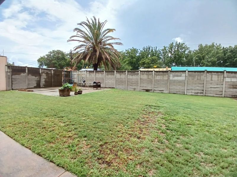 Spacious backyard featuring a large lawn area, a concrete patio section, and a secure precast concrete boundary wall.