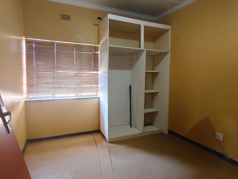 An empty bedroom featuring a built-in wardrobe, venetian blinds, and ceiling cornice, requiring cosmetic updates to the flooring and wall finishes.