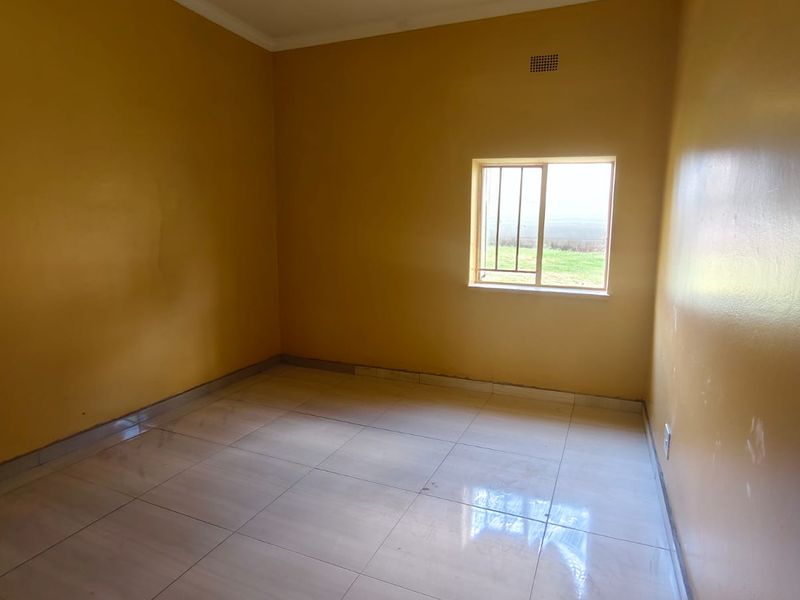 An empty bedroom featuring tiled flooring, yellow painted walls, and a window fitted with security bars.