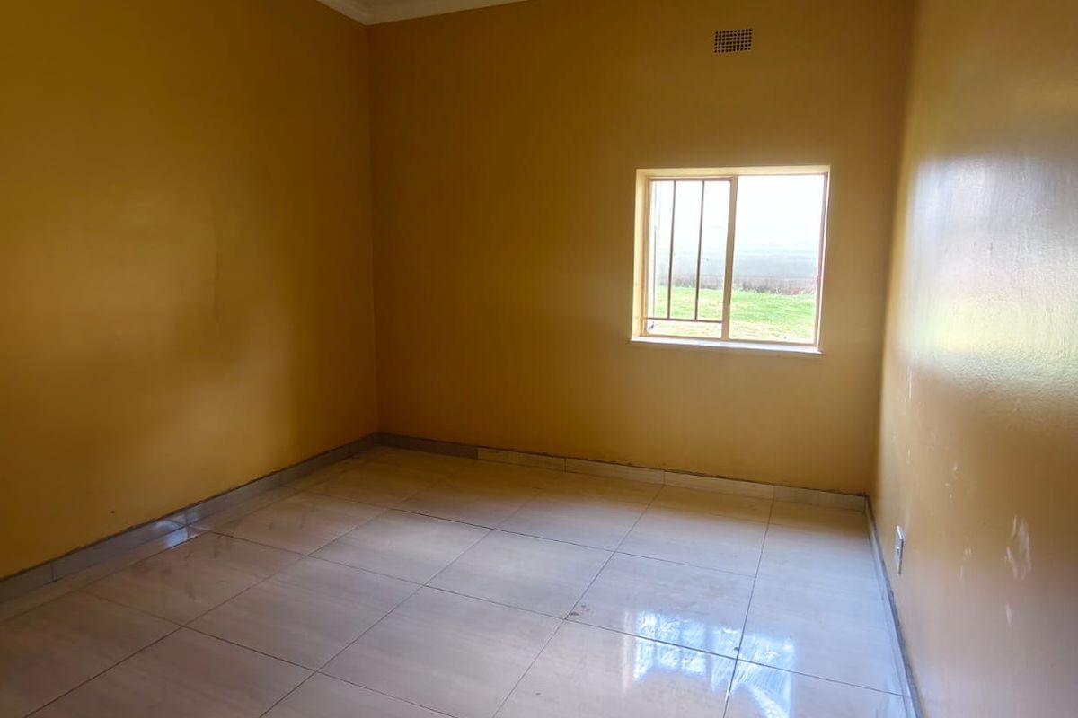 An empty bedroom featuring tiled flooring, yellow painted walls, and a window fitted with security bars.