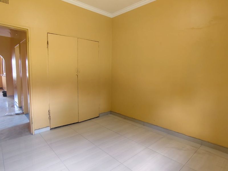 An empty bedroom featuring neutral tiled flooring, built-in cupboards, and simple ceiling cornicing, providing a clean canvas for personalization.