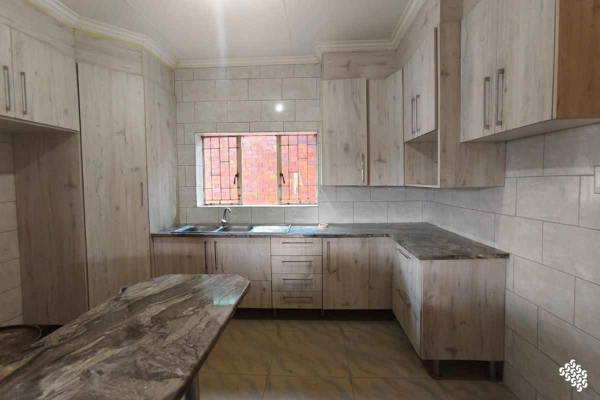 A clean and modern kitchen featuring light wood-grain cabinetry, stone-look countertops, a double sink, and neutral wall tiling.