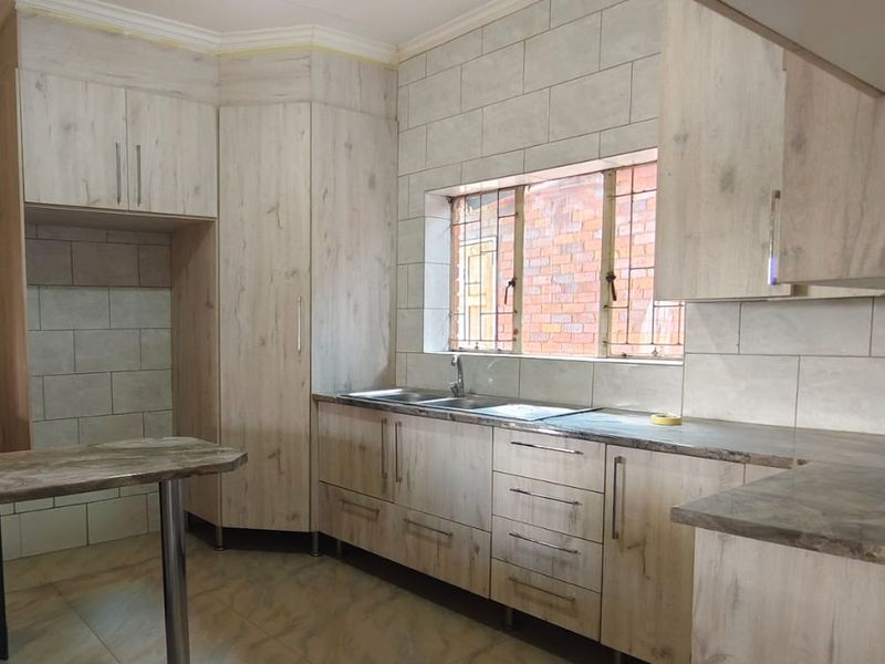 A functional kitchen featuring light wood-grain cabinetry, tiled backsplash, and tiled flooring, currently awaiting final finishing touches and appliance installation.