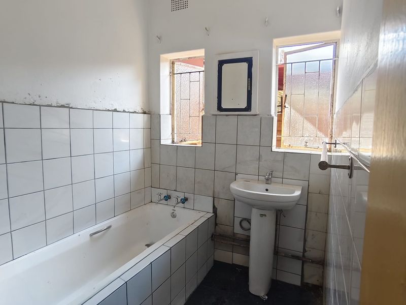 A dated bathroom featuring a bathtub and pedestal basin, requiring renovation and repair to the wall tiling and exposed plumbing fixtures.