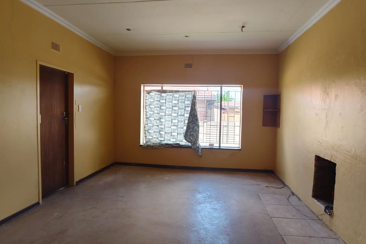 An empty living room featuring a built-in fireplace, coved ceilings, and security bars on the window, requiring cosmetic updates and flooring repairs.