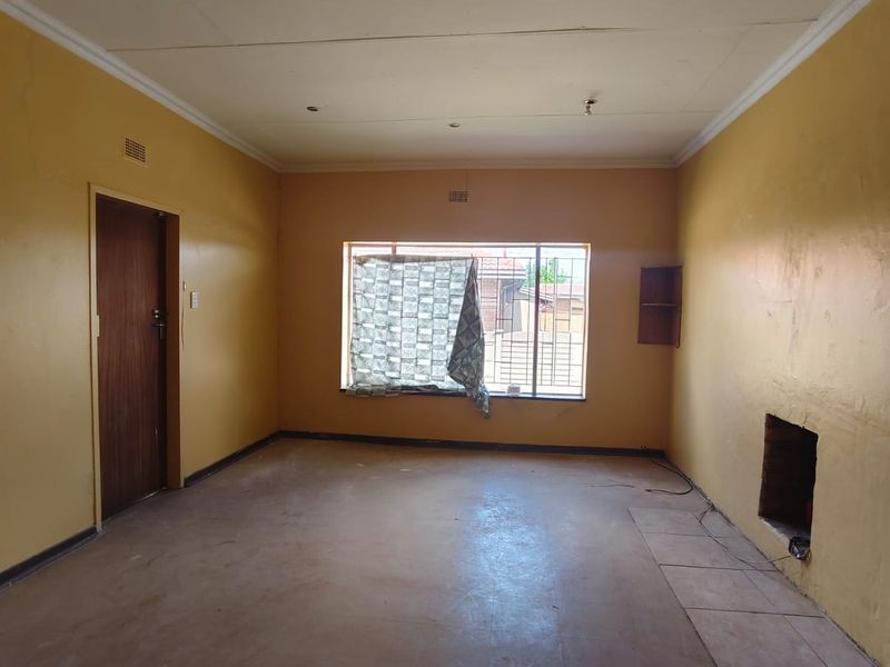 An empty living room featuring a built-in fireplace, coved ceilings, and security bars on the window, requiring cosmetic updates and flooring repairs.