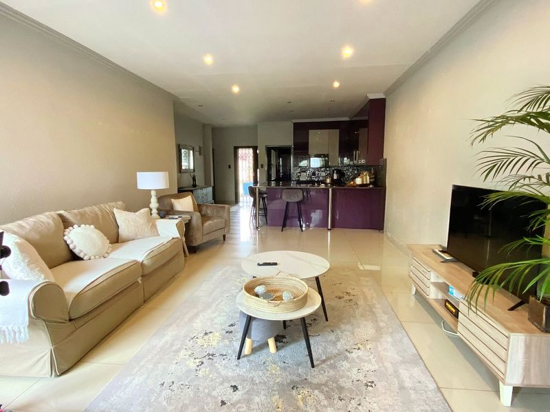 An open-plan living area featuring tiled floors, recessed lighting, and a modern kitchen with a central island and dark cabinetry.