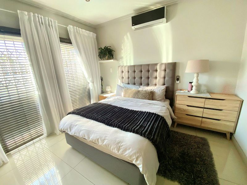 A well-maintained bedroom featuring tiled flooring, a wall-mounted split-system air conditioner, and sliding glass doors with integrated blinds providing natural light.