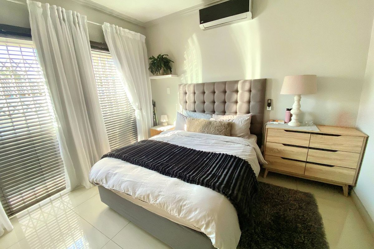 A well-maintained bedroom featuring tiled flooring, a wall-mounted split-system air conditioner, and sliding glass doors with integrated blinds providing natural light.