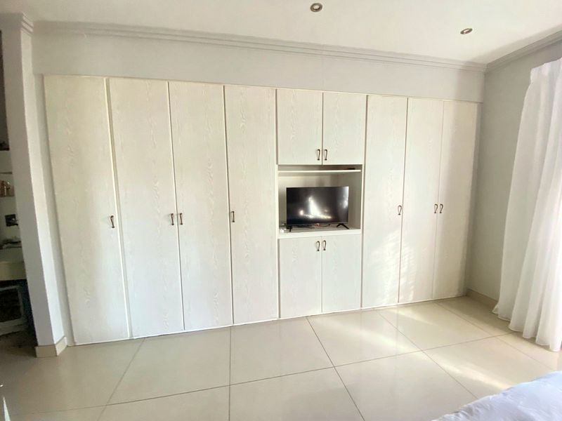 A bedroom featuring extensive floor-to-ceiling built-in cupboards with a central media niche, complemented by neutral tiled flooring and recessed ceiling lighting.