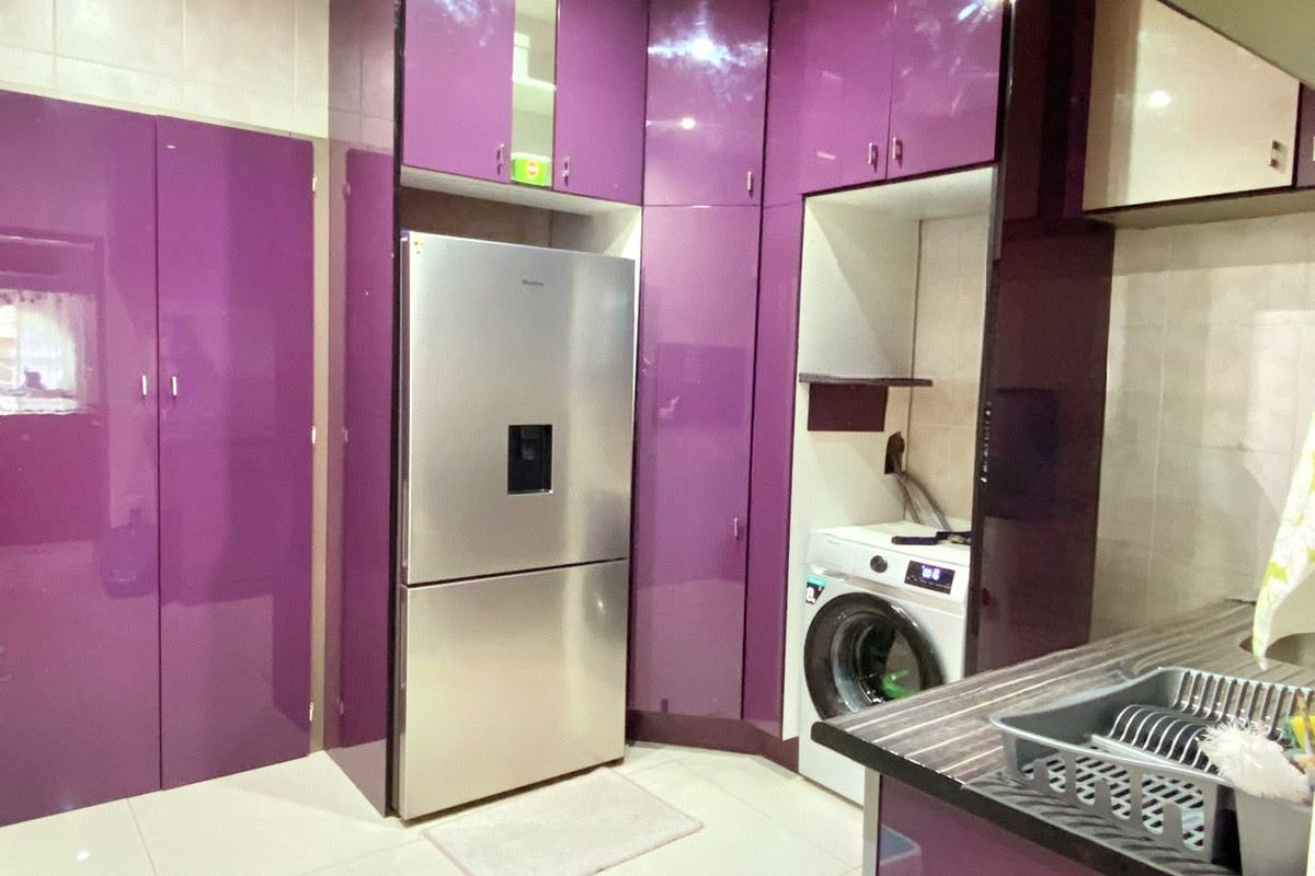 Modern kitchen featuring high-gloss purple cabinetry, integrated appliance spaces, and tiled flooring, offering a bold and functional culinary workspace.