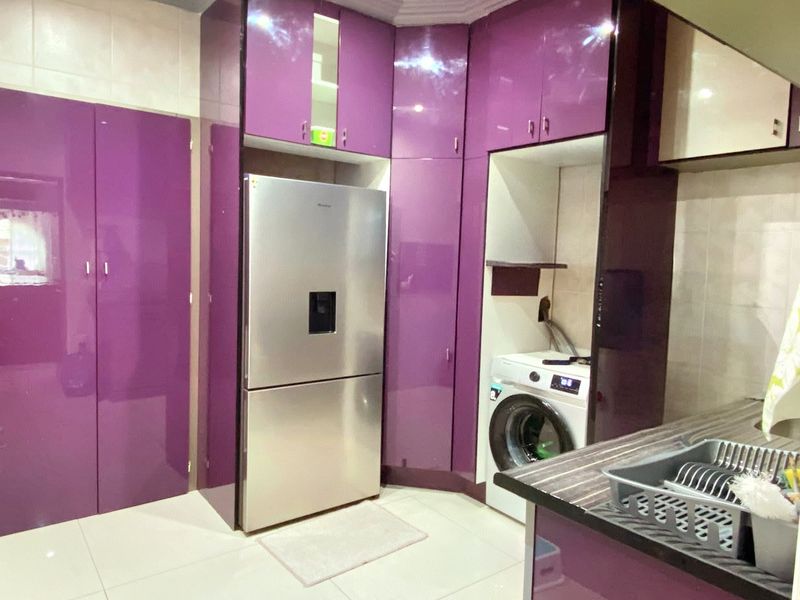 Modern kitchen featuring high-gloss purple cabinetry, integrated appliance spaces, and tiled flooring, offering a bold and functional culinary workspace.