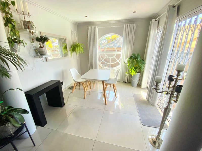 Bright dining area featuring large porcelain floor tiles, recessed downlighting, and a distinctive arched window with access to the exterior via a security gate.