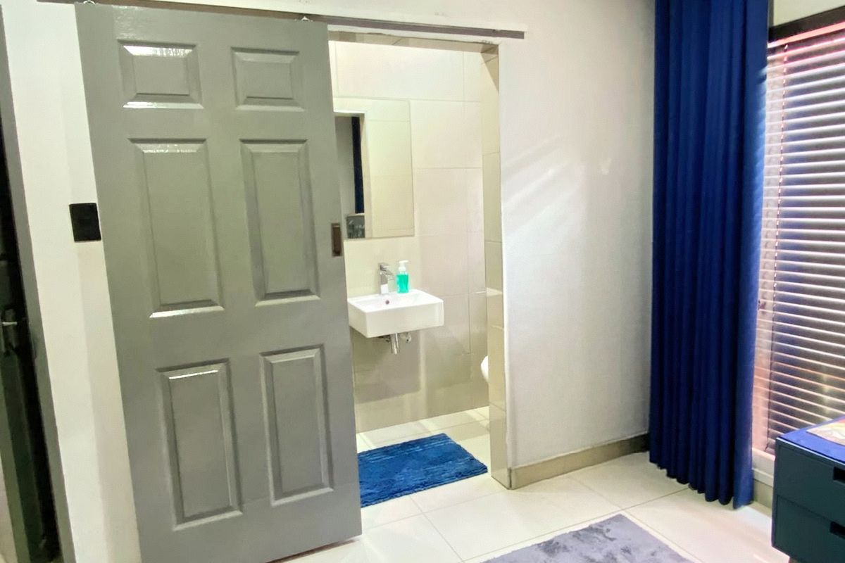 A compact bathroom featuring a wall-mounted basin and tiled finishes, accessed via a grey sliding door from the adjacent room.