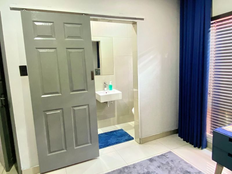 A compact bathroom featuring a wall-mounted basin and tiled finishes, accessed via a grey sliding door from the adjacent room.