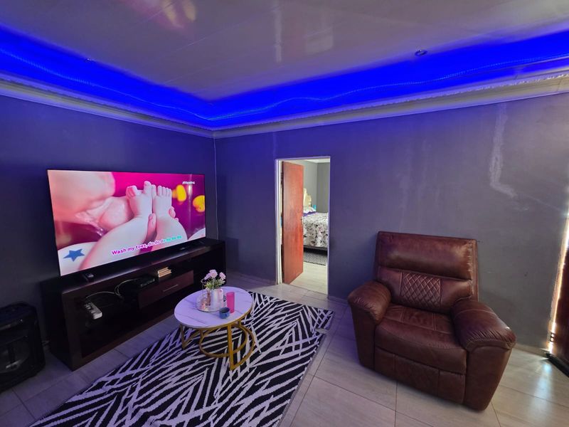 Living room featuring tiled flooring and decorative recessed ceiling lighting with blue LED accents, showing signs of wall surface wear.