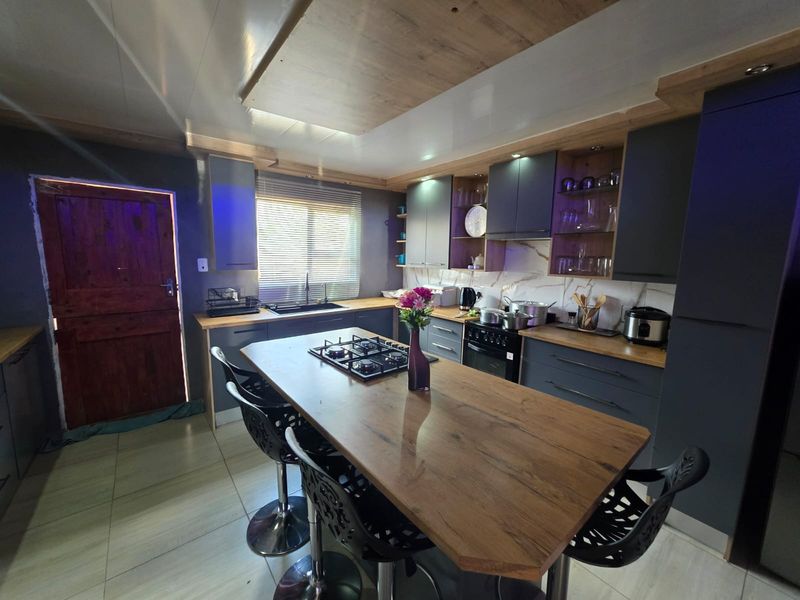 Modern kitchen featuring dark cabinetry, a central island with a built-in gas hob, stone-look backsplash, and integrated appliances.