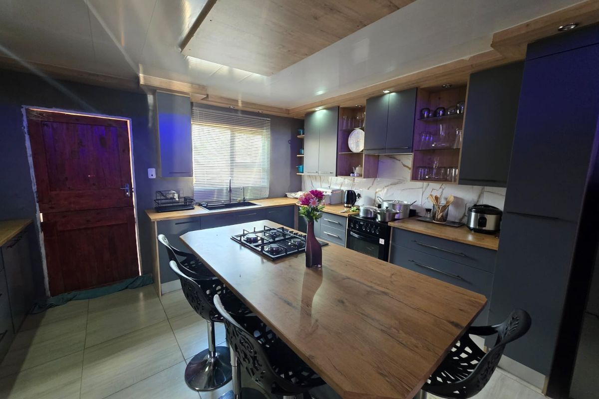 Modern kitchen featuring dark cabinetry, a central island with a built-in gas hob, stone-look backsplash, and integrated appliances.